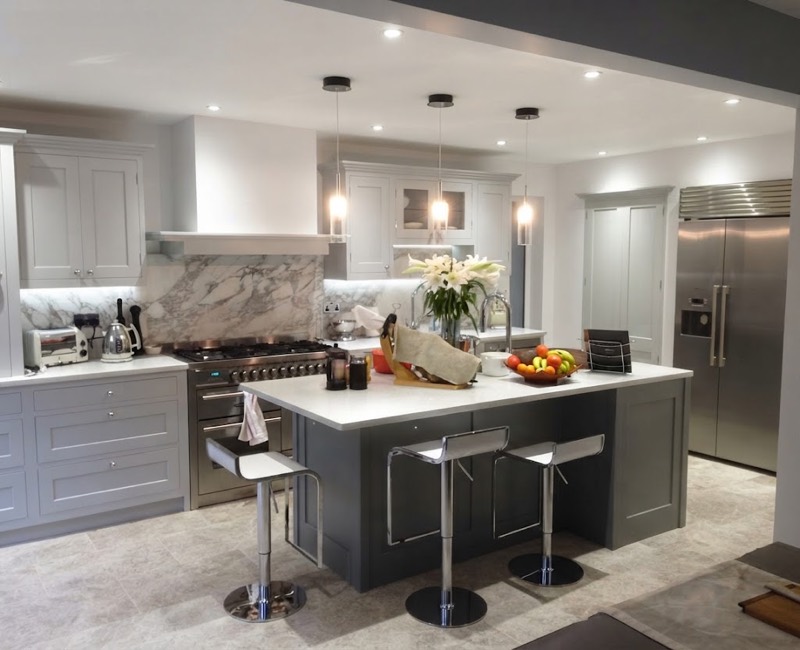 Hand-painted grey shaker kitchen with a marble splashback, a stainless range cooker and a dark grey island with three chrome stools.