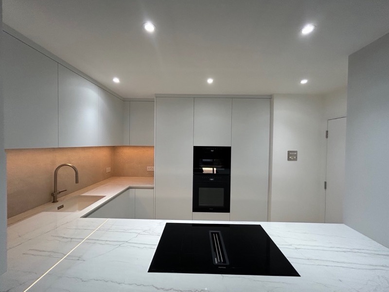 Compact white handleless kitchen, newly finished and unfurnished, with a marble-effect island, brass tap and integrated ovens.